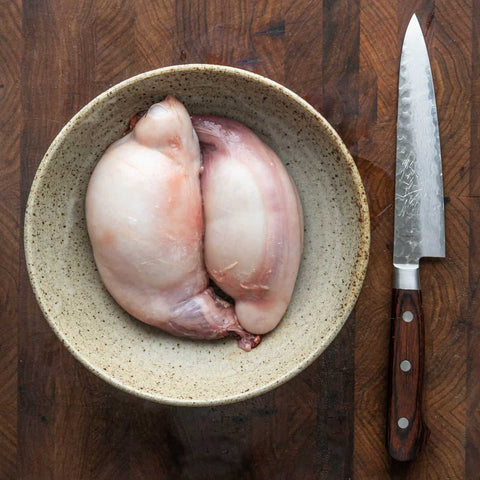 a raw chicken in a bowl next to a knife