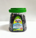 Ikram Natural Black Olives packaging featuring a transparent container with a green lid, showcasing the dark olives inside. The label includes the product name in English and additional translations, highlighting the net weight of 24.69 ounces (700g). The background is plain, emphasizing the product.