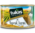 Tukaş stuffed vine leaves in a can, featuring a picturesque countryside background and the brand logo prominently displayed. The label reads 'Yaprak Sarma' indicating the product type.