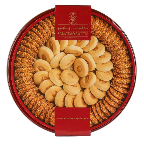 An elegant close-up of a round red tin containing Zalatimo Sweets, displaying an array of sesame and butter cookies. The cookie assortment is meticulously presented, highlighting the rich colors and textures of the cookies, making it an enticing treat for celebrations and gifts.